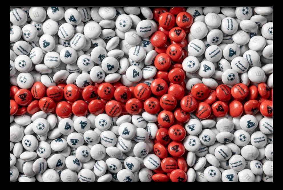 Dulces de M&M'S blancos y rojos formando la bandera de Inglaterra, con balones de fútbol, trofeos y el texto "Come on England!" impresos.