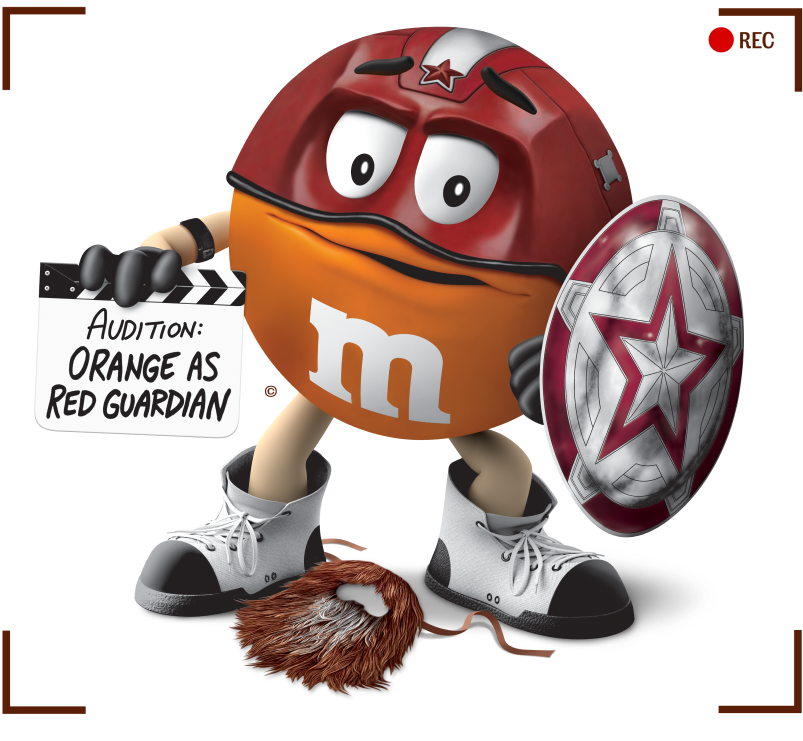 M&M's arancione vestito da Red Guardian, con un cartello con scritto 'Casting per Red Guardian'