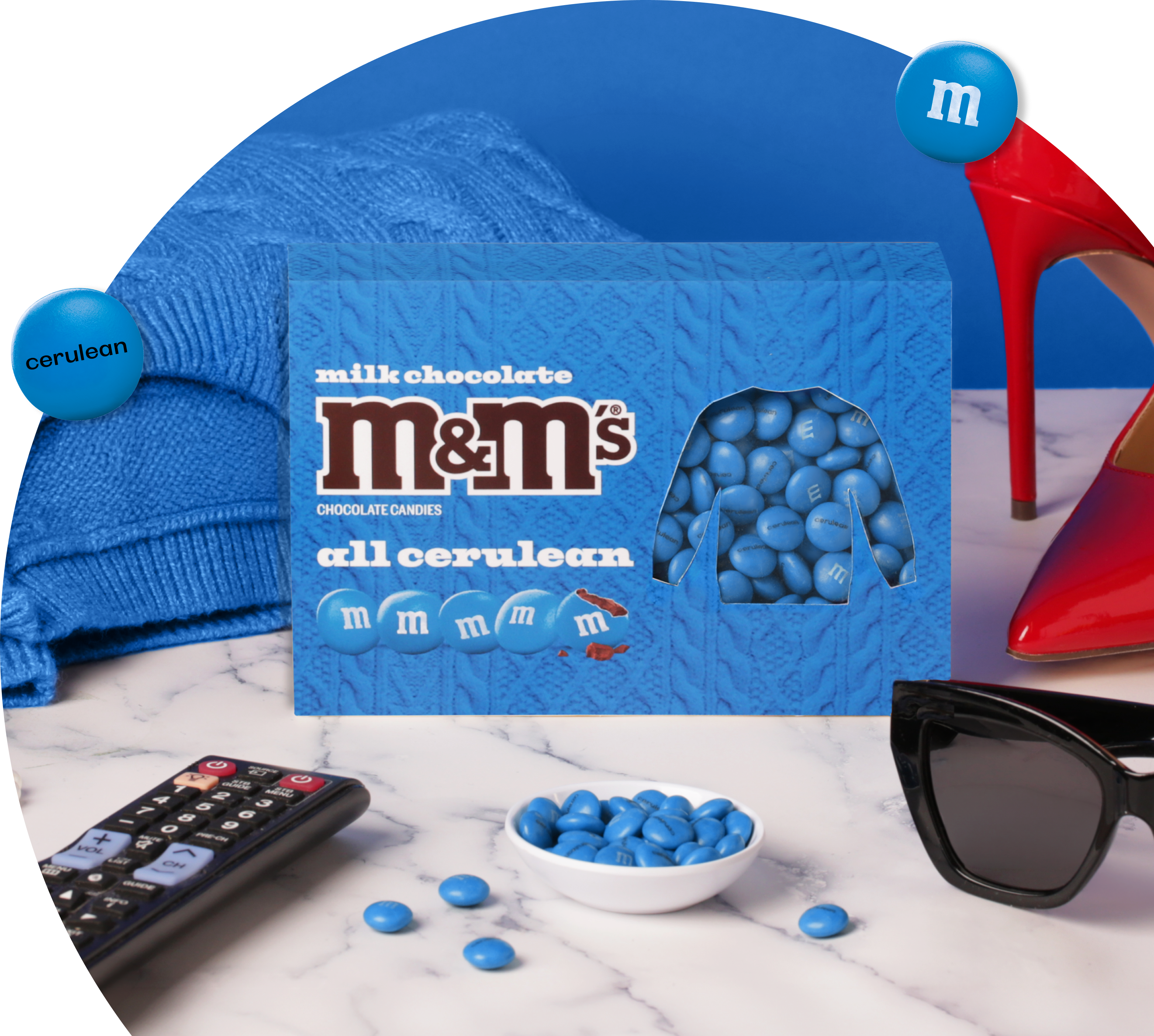 M&M'S cerulean limited edition pack with sweater-inspired design, accessories, and candies on marble.