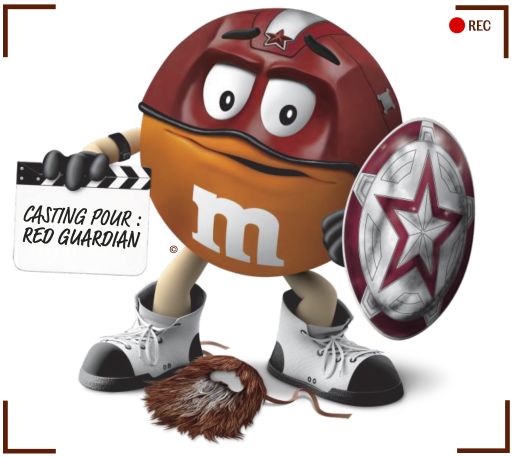 M&M’s orange déguisé en Red Guardian, tenant un clap sur lequel est écrit ‘Casting pour Red Guardian'