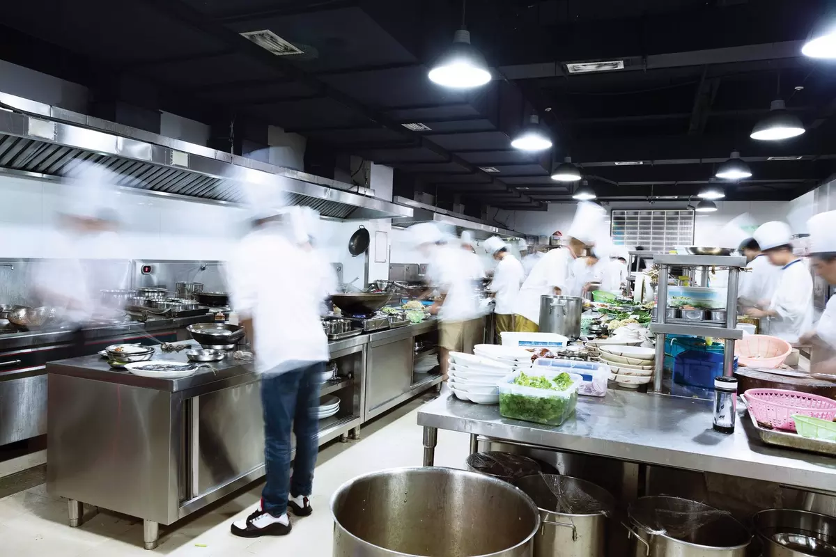 Chefs working in a busy commercial kitchen with stainless steel counters and cooking stations.