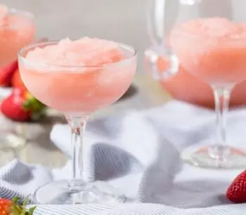 Three frosty pink drinks in coupe glasses with strawberries nearby.