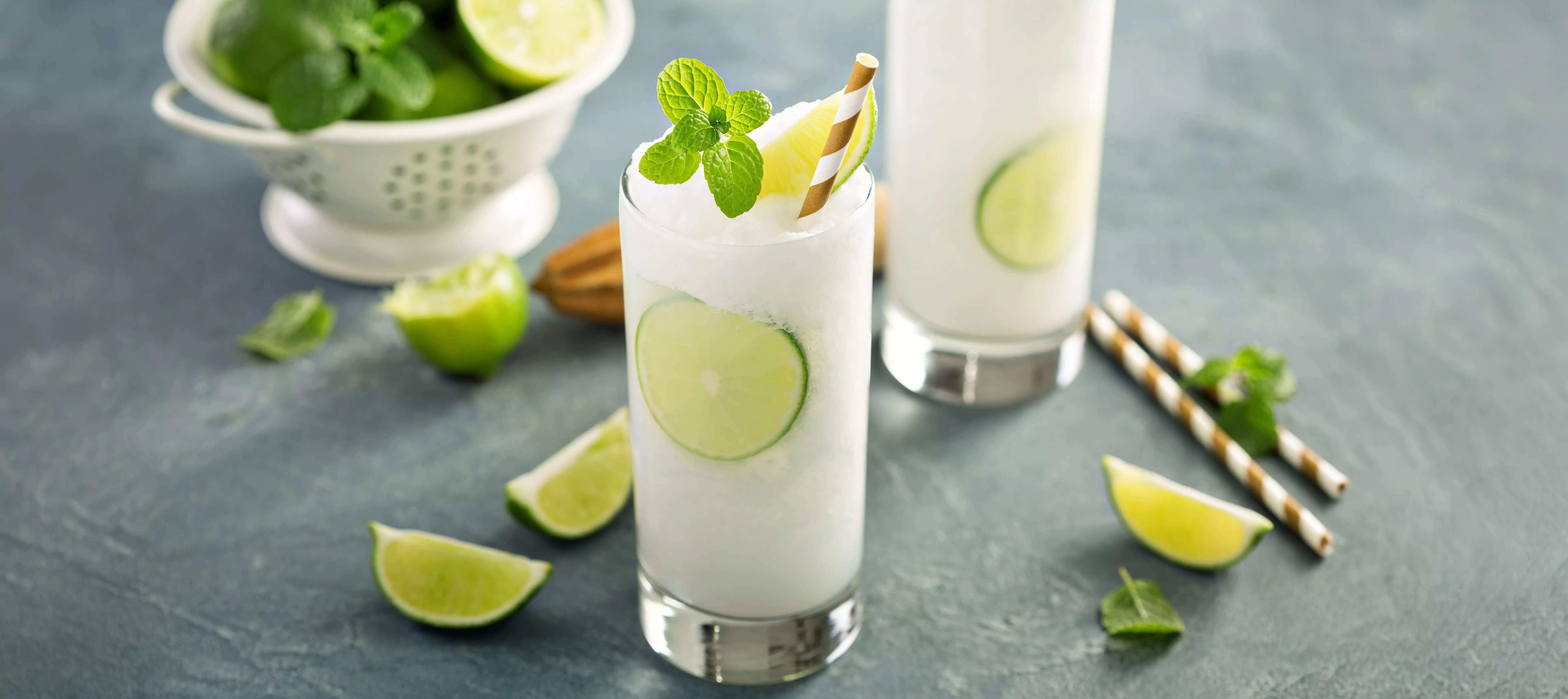 Two glasses of frozen lime drink with mint garnish and striped straw.
