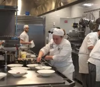 Chefs in a commercial kitchen preparing dishes, wearing white uniforms and hats.
