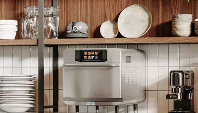 Countertop oven with touchscreen display on kitchen counter beside an espresso machine.
