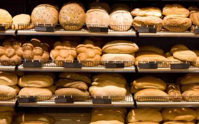 Various types of bread arranged on shelves in a bakery.