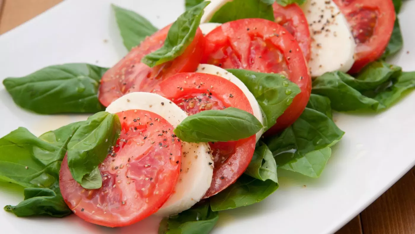 Caprese salad with sliced tomatoes, mozzarella, basil, and pepper on a white plate.
