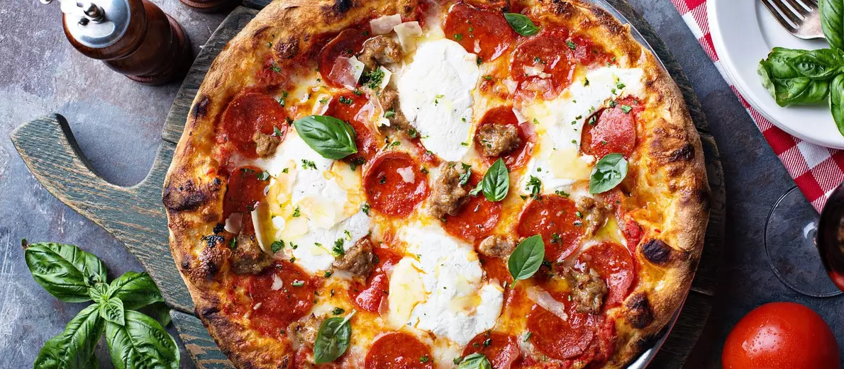 Pepperoni pizza with cheese, sausage, and basil on a wooden serving board.