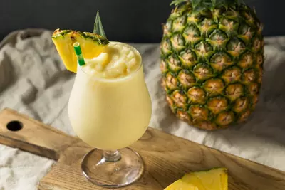 Frozen pineapple smoothie in a glass with a straw and pineapple wedge garnish.
