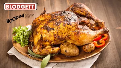 Roasted chicken on a platter with potatoes, red peppers, and herbs. Blodgett and Hoodini logos visible.