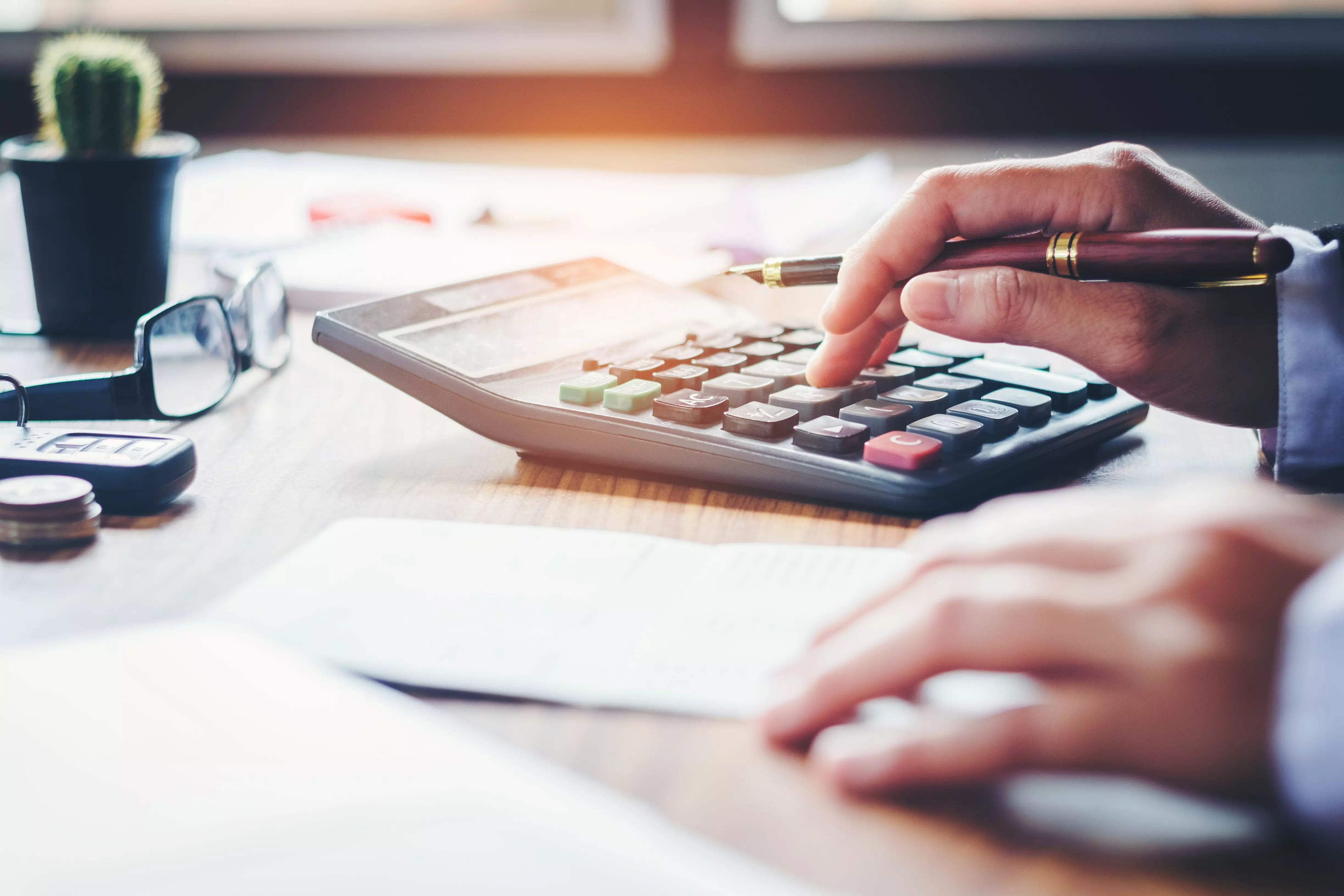 Hand holding a pen while pressing buttons on a calculator at a desk.