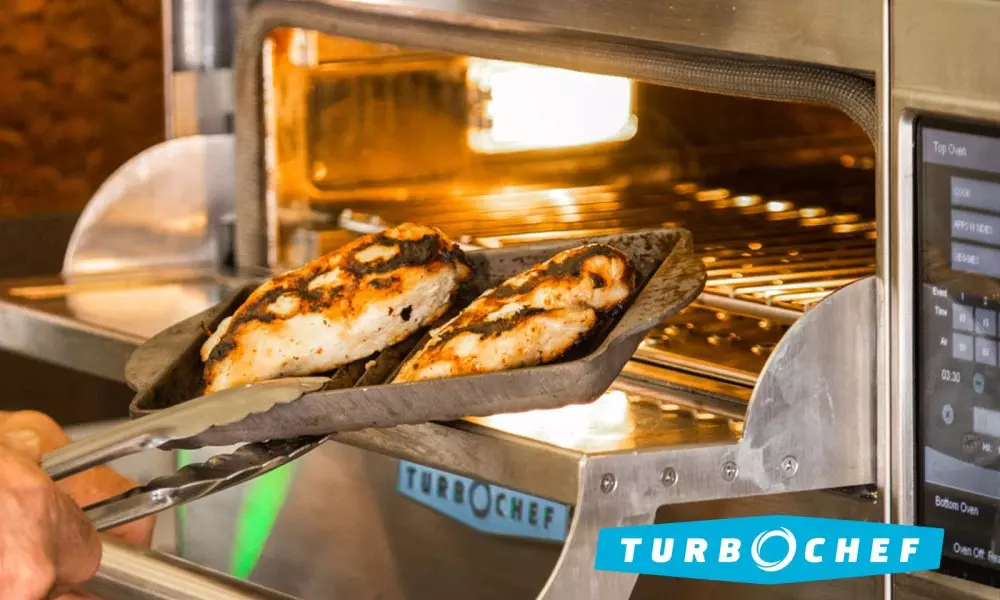 Grilled chicken being removed from a TurboChef oven using tongs.