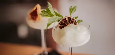 Cocktail in a coupe glass topped with mint leaves and a dried citrus slice.