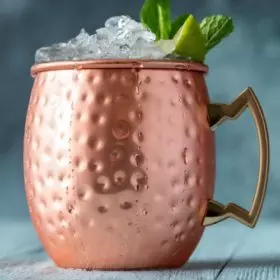 Copper mug with ice, lime wedge, and mint leaves on top.