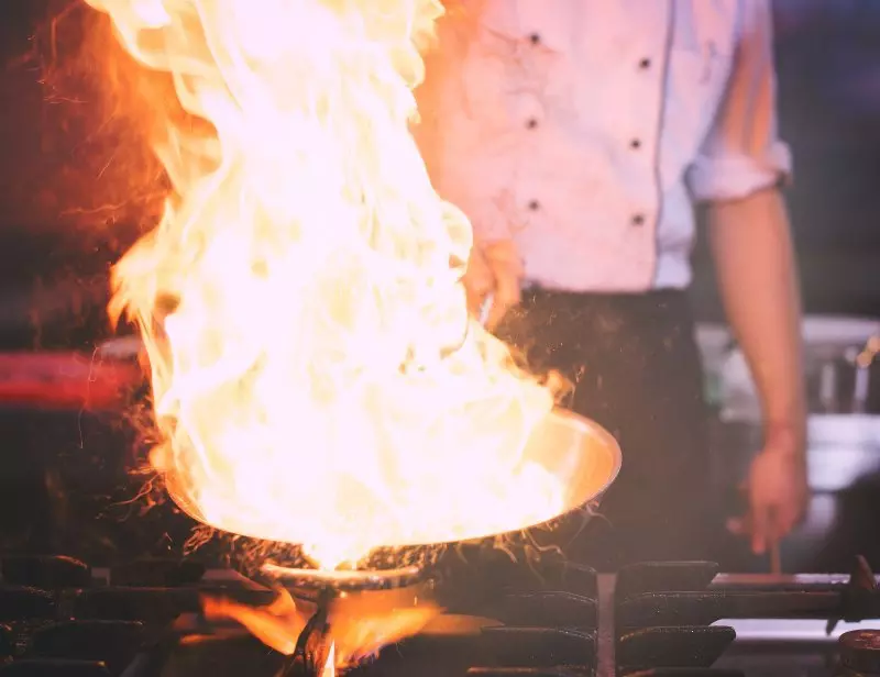 Chef cooking with large flames in a pan on a stove.