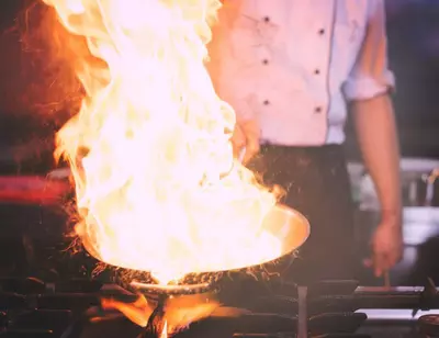 Chef cooking with large flames in a pan on a stove.