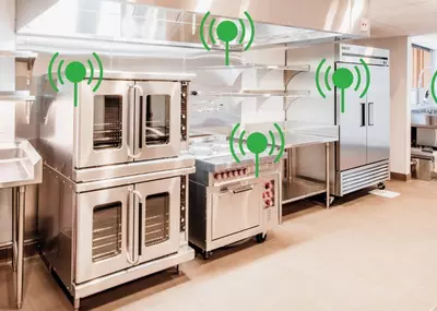 Commercial kitchen with ovens, range, fridge, and green Wi-Fi symbols.