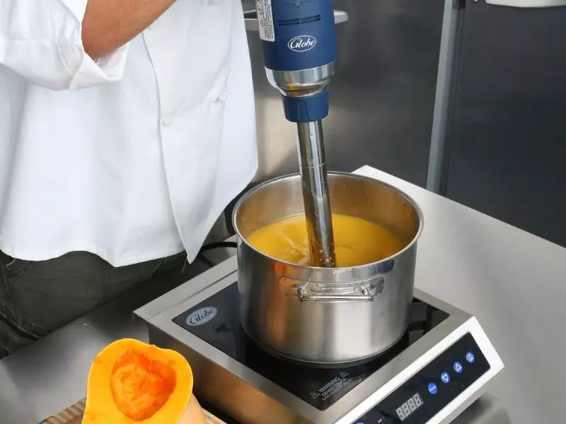 Chef blending soup in a pot with a Globe immersion blender on an induction cooktop.