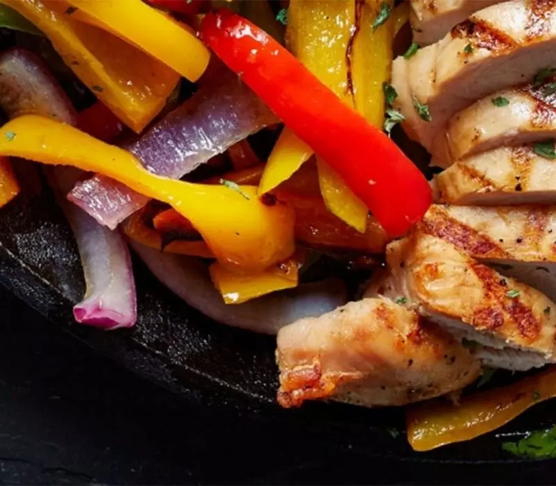 Grilled chicken slices with sautéed red, yellow peppers, and onions on a skillet.