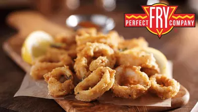 Fried calamari on a wooden board with lemon. Perfect Fry Company logo displayed.