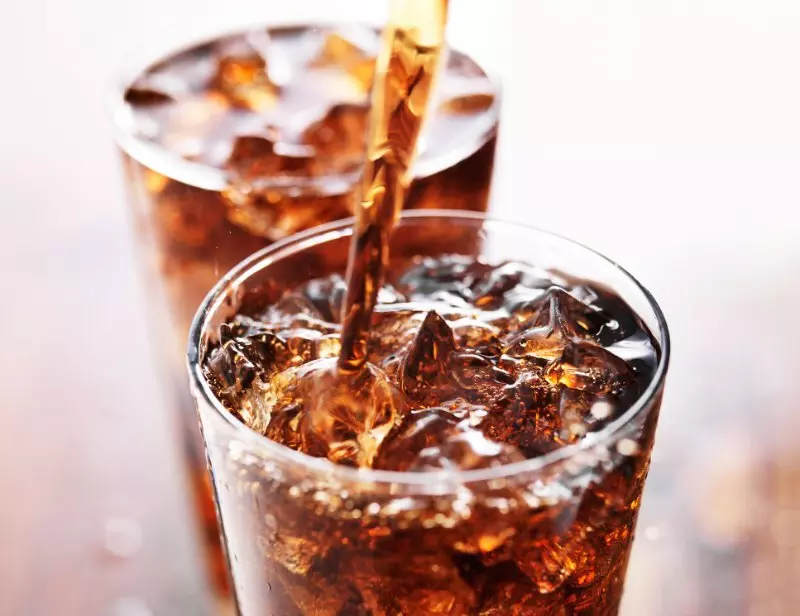 Two glasses filled with cola and ice cubes, one being poured.