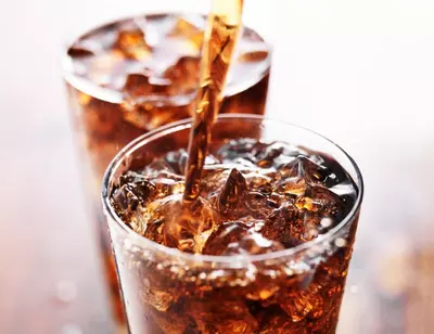 Two glasses filled with cola and ice cubes, one being poured.