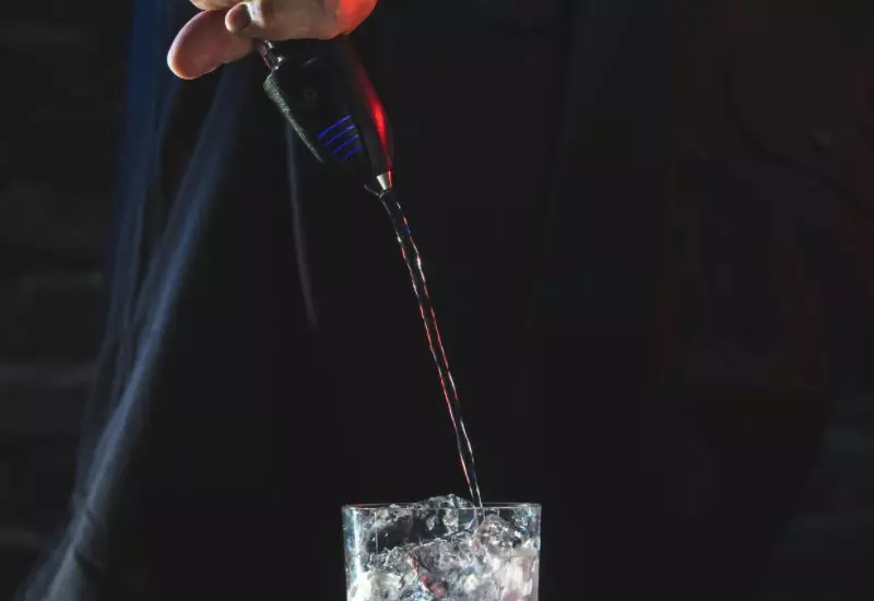 Liquor being poured into a glass with ice cubes using a pour spout.