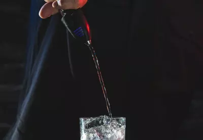 Liquor being poured into a glass with ice cubes using a pour spout.