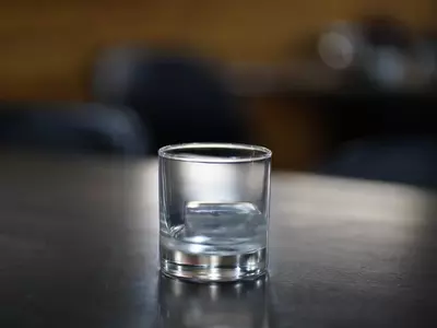 Empty glass with a single ice cube on a table.