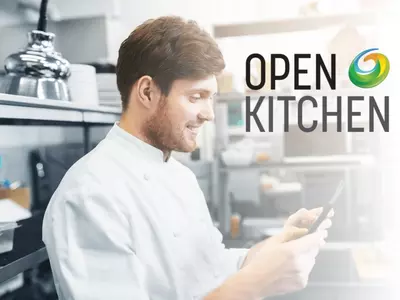 Chef in white uniform using a tablet, with "Open Kitchen" logo in background.