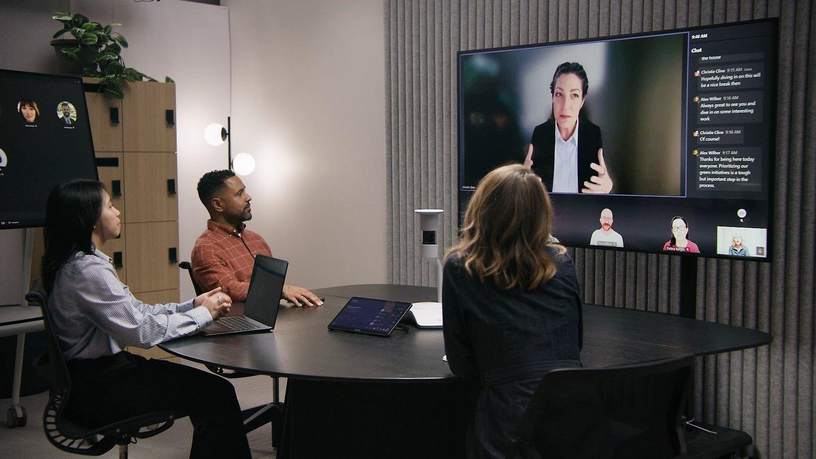 trois personnes assises à une table avec un ordinateur portable et un appel en visioconférence
