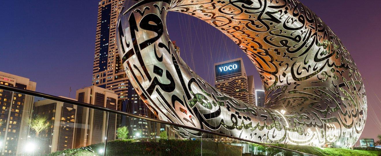 a large metal sculpture is sitting in front of a city skyline