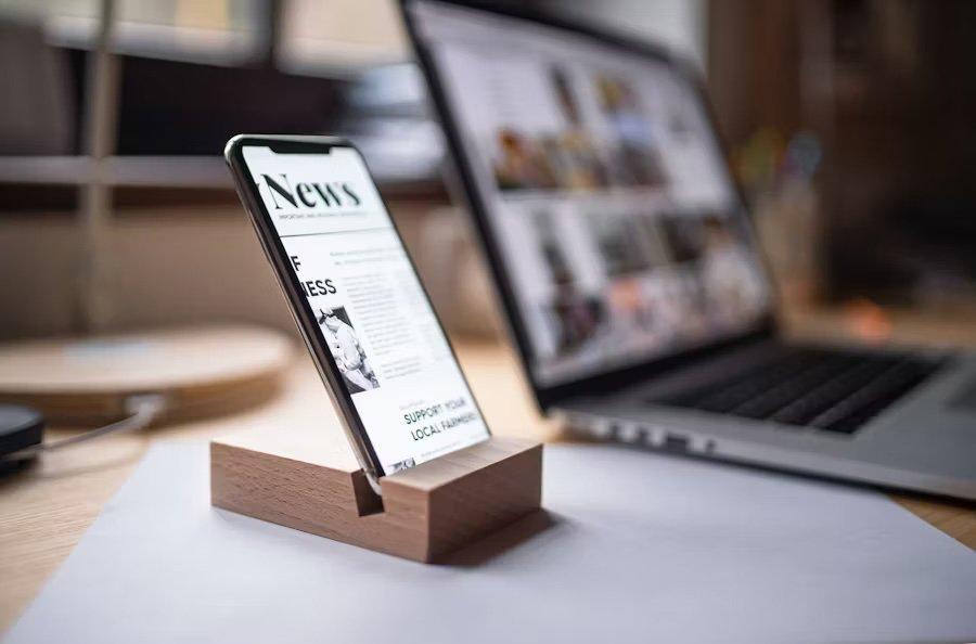 a cell phone sitting on a wooden stand next to a laptop