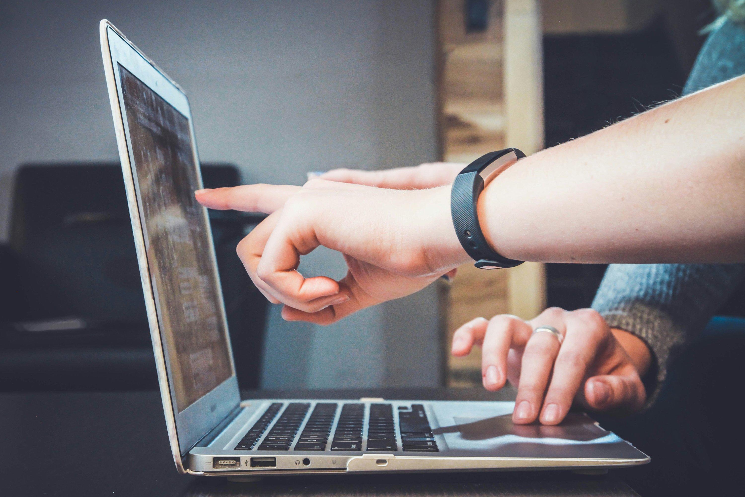 a person pointing at a laptop computer screen with their finger