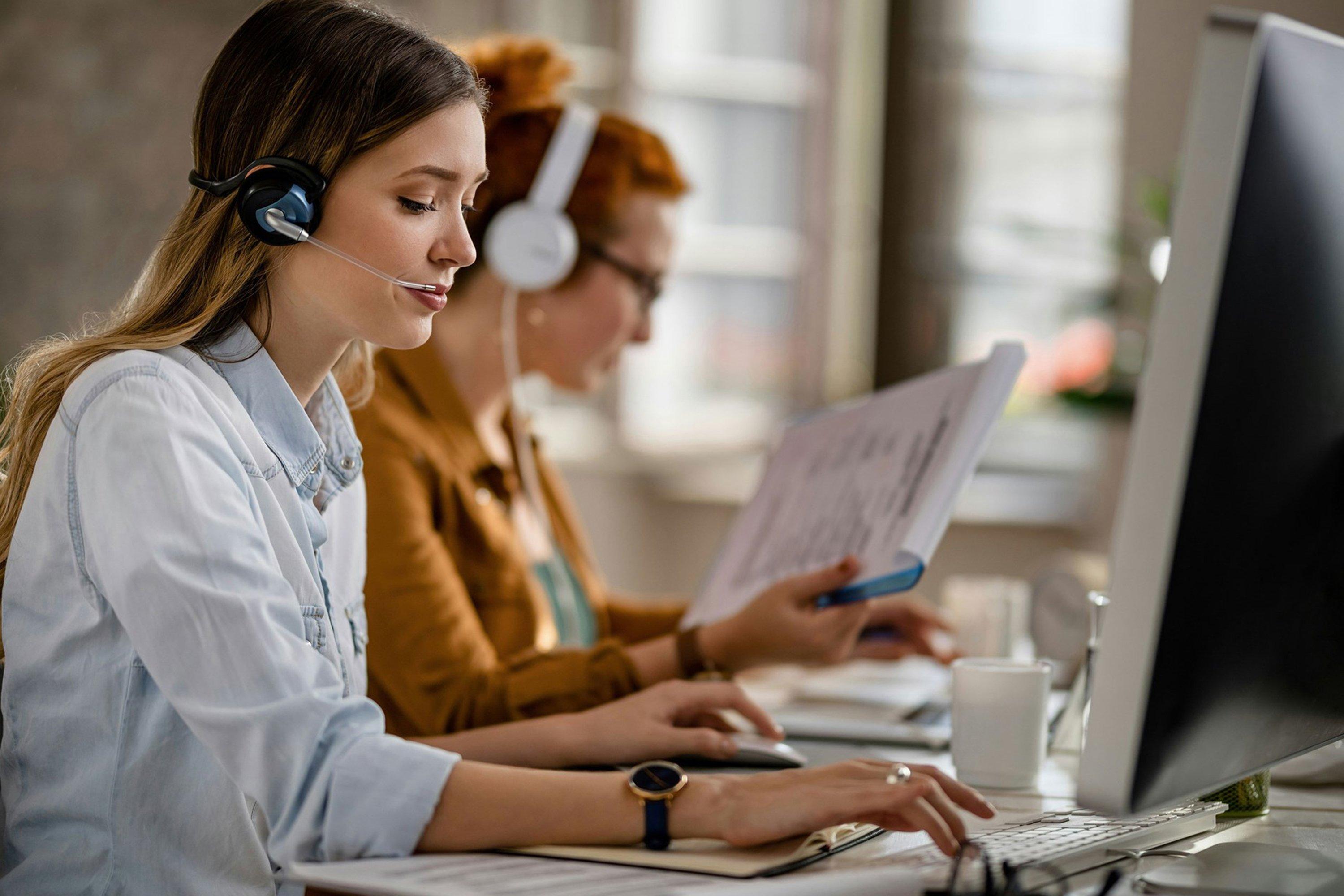 two women in headsets working on computers in a room