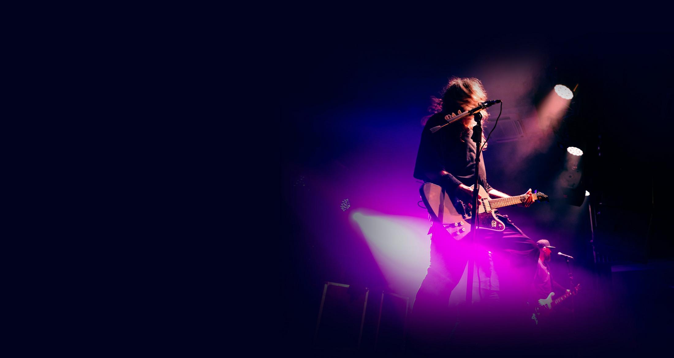 un homme sur scène avec une guitare et des lumières violettes