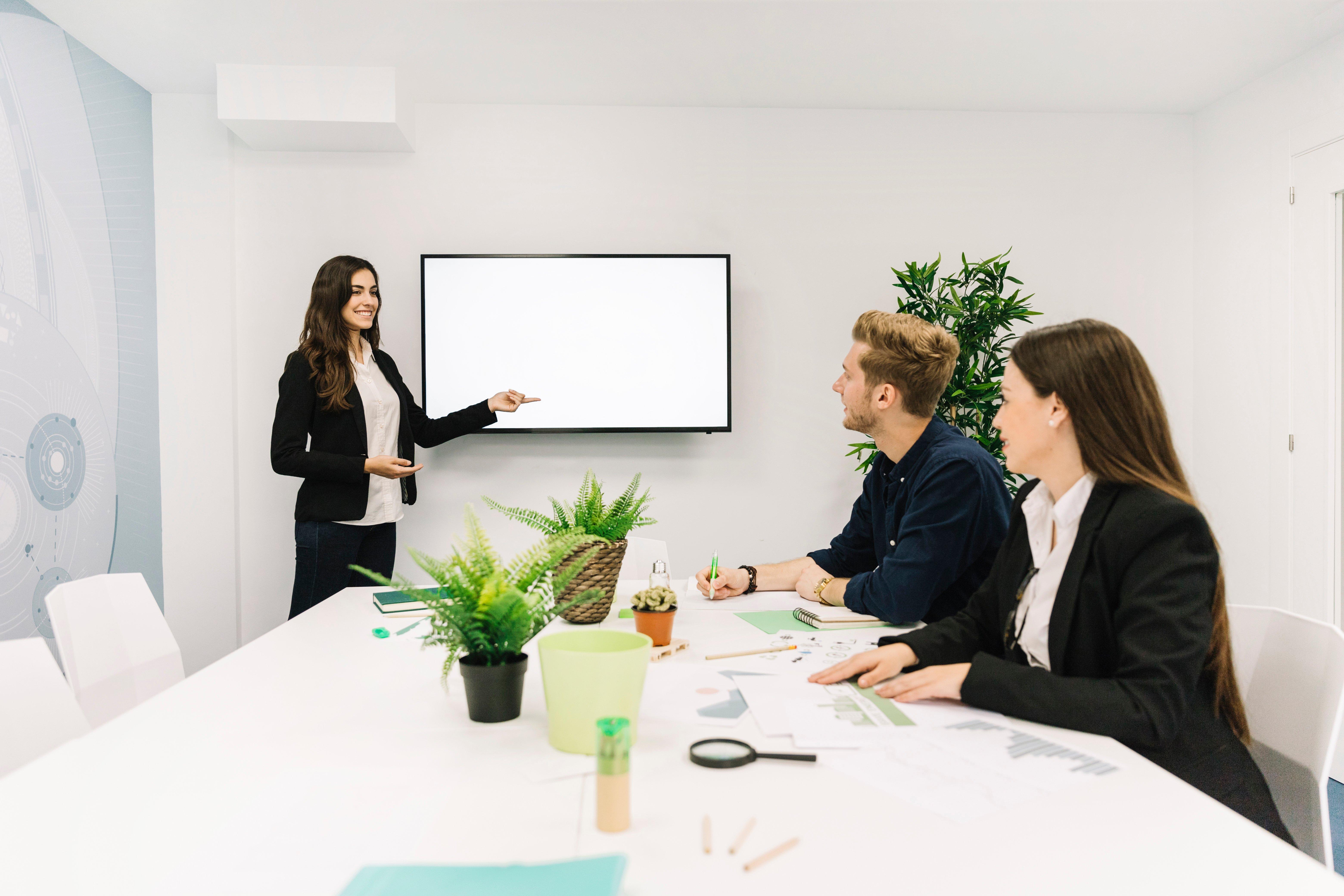 a group of people sitting around a conference table with a large screen