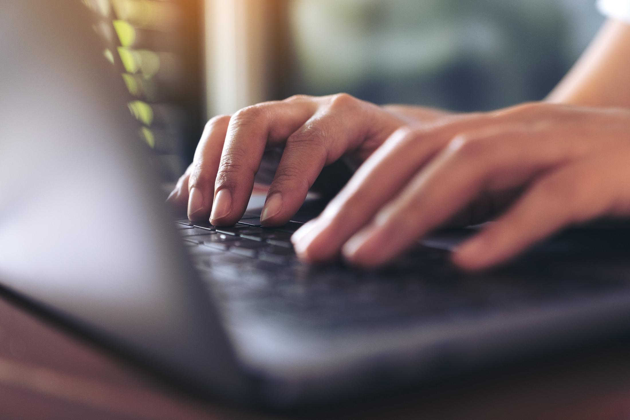une personne tapant sur un ordinateur portable, les mains sur le clavier