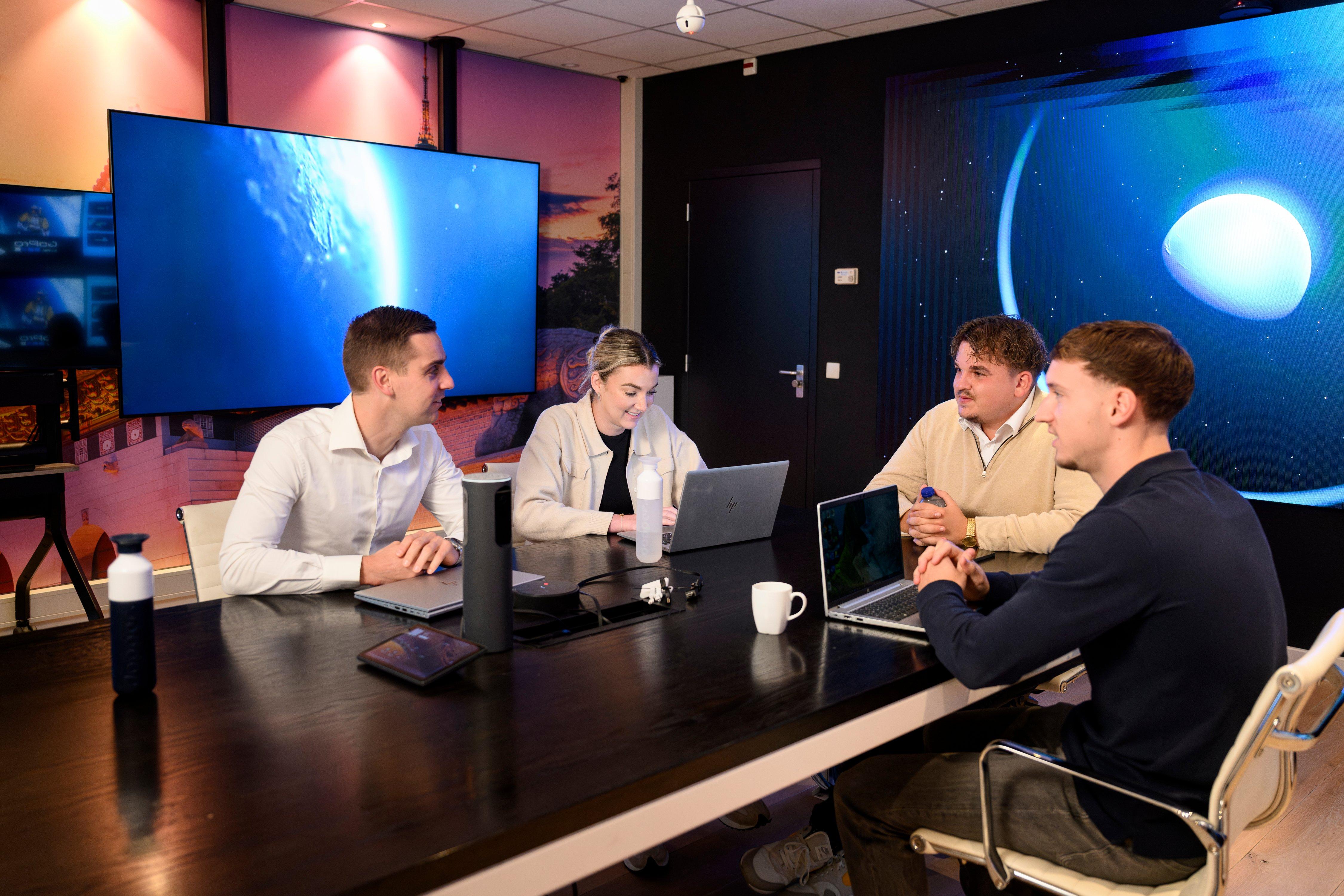 a group of people sitting around a table with laptops