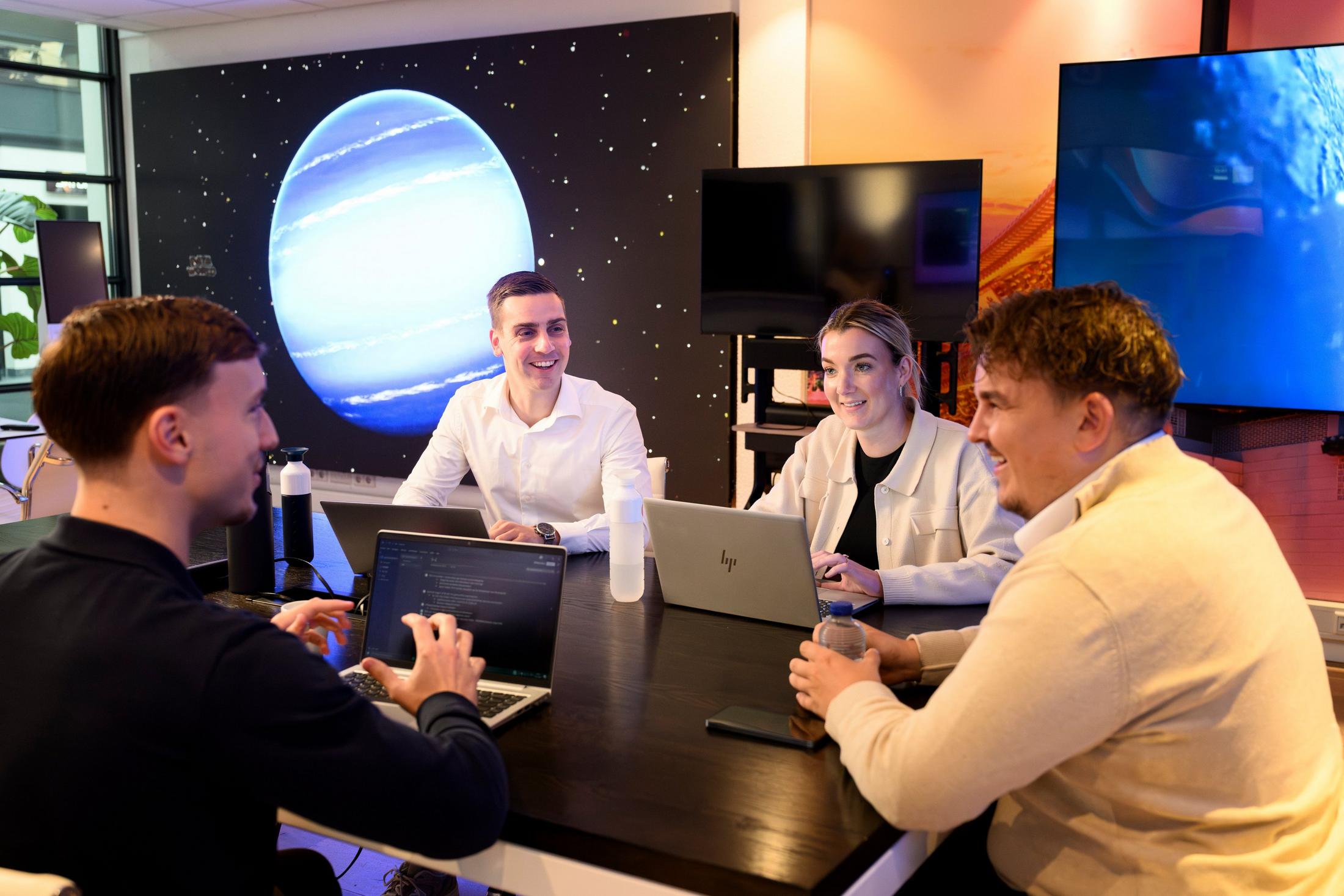 a group of people sitting around a table with laptops