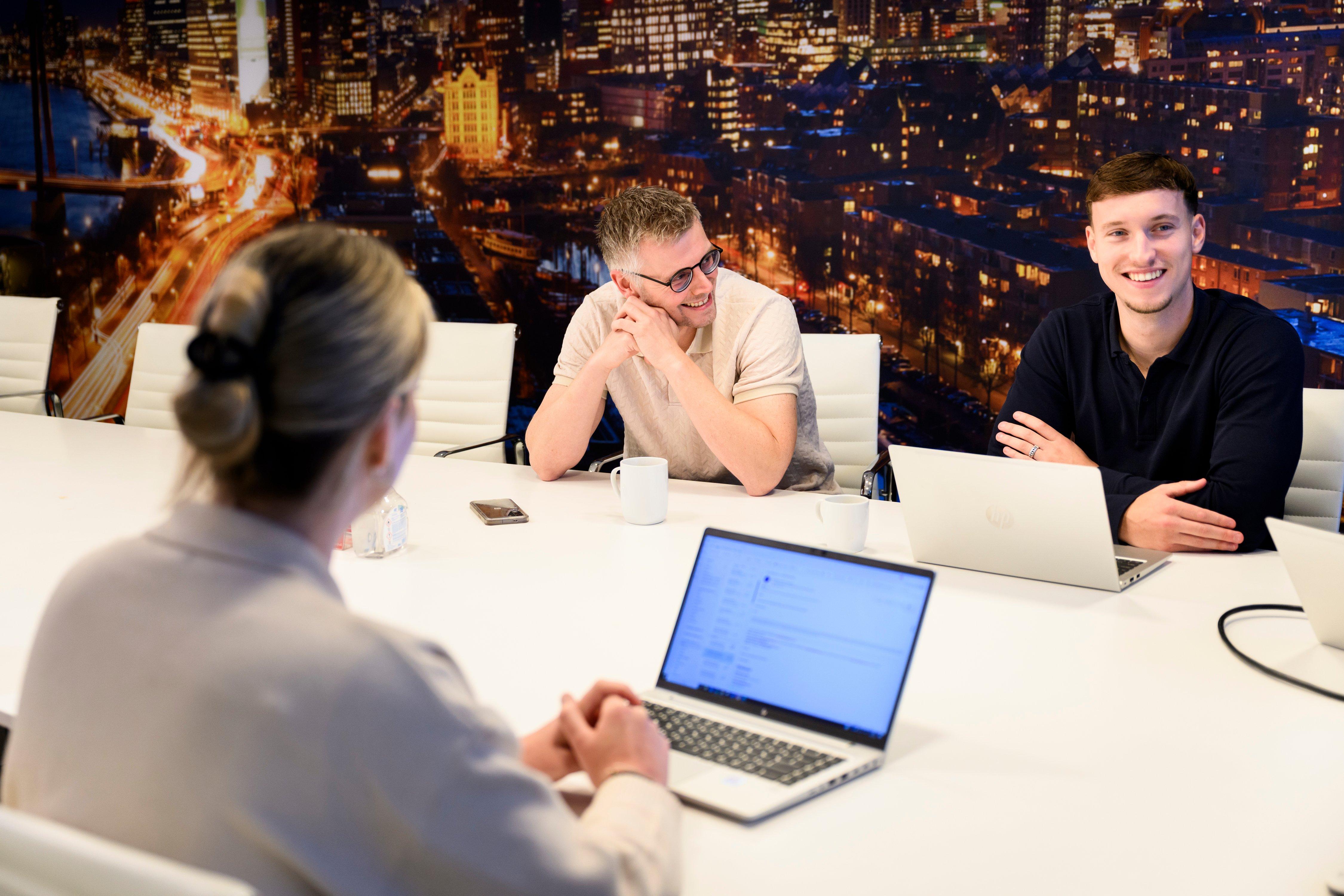 three people sitting at a table with laptops and a city skyline in the background