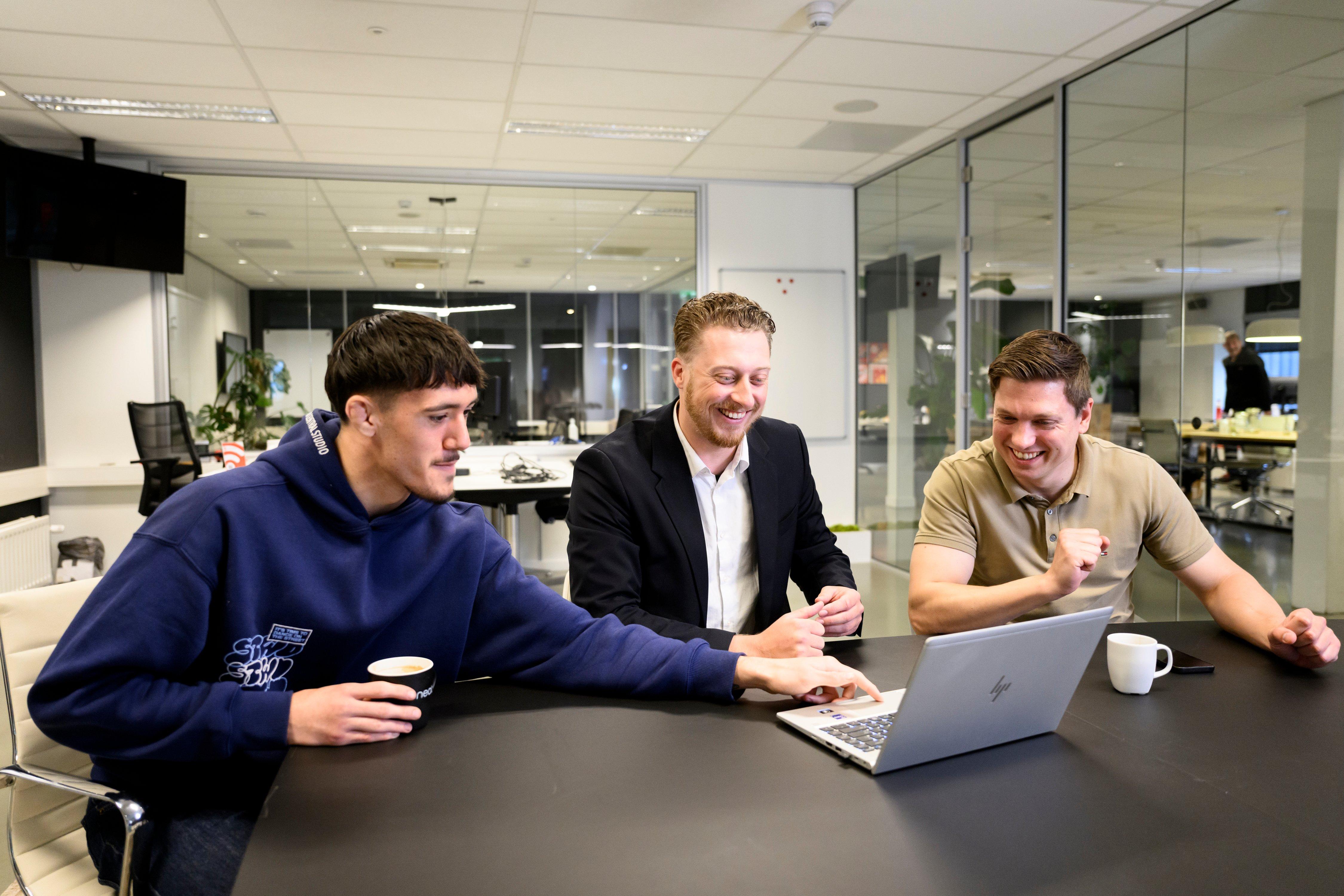three men sitting at a table with a laptop computer