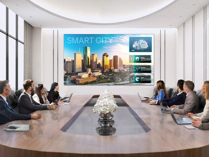 a group of people sitting around a conference table with a large screen