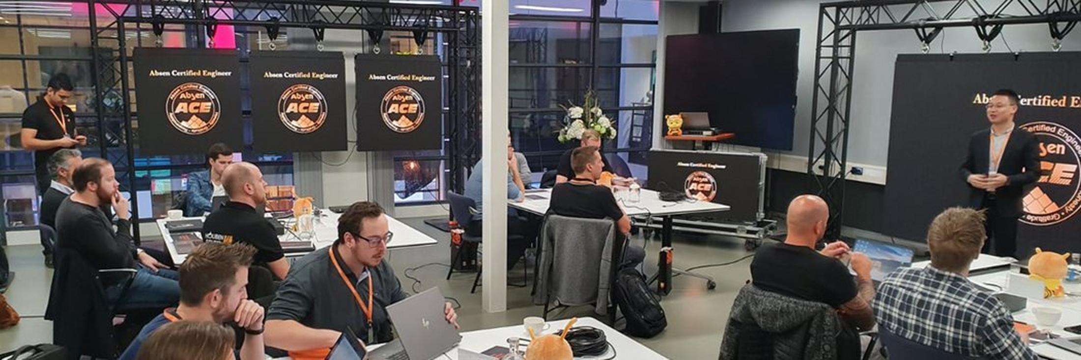 a group of people sitting at tables with laptops and a man standing in front of them