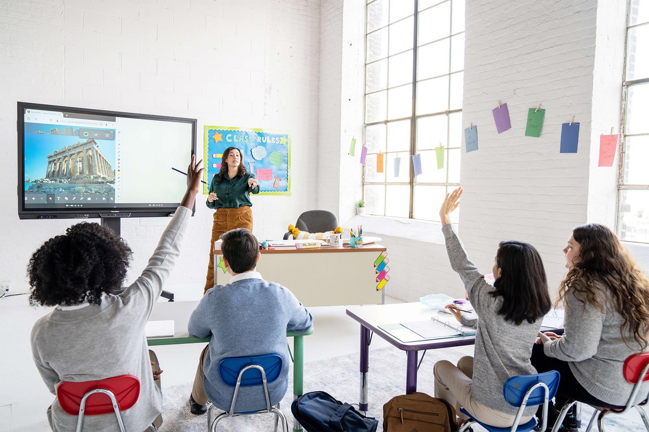 a group of students sitting in a classroom with their hands up