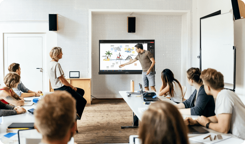 a group of people sitting around a table watching a man on a screen
