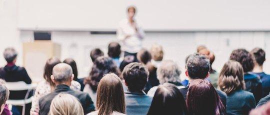 a group of people sitting in a room listening to a speaker