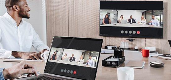 a man sitting at a desk with a laptop and a man on a video call