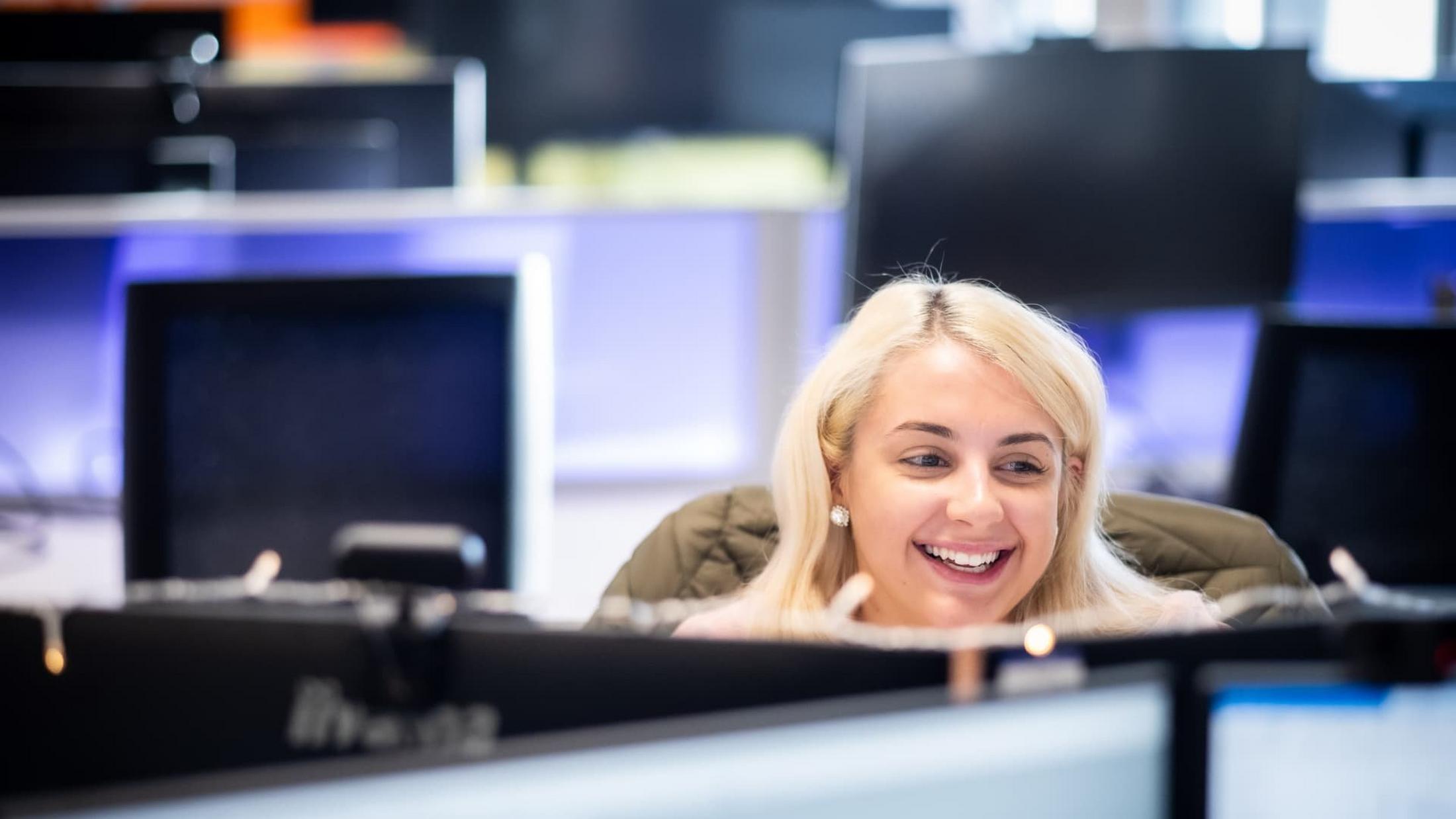 a woman smiling while sitting at a computer desk