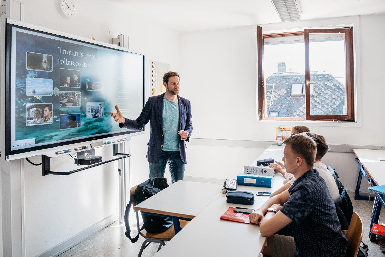 a man standing in front of a large screen in a classroom